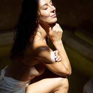 Body wrapping to jedna z metod, która pomaga zadbać o gładką i jędrną skórę. Na zdjęciu kobieta nakłada kosmetyki na skórę. 